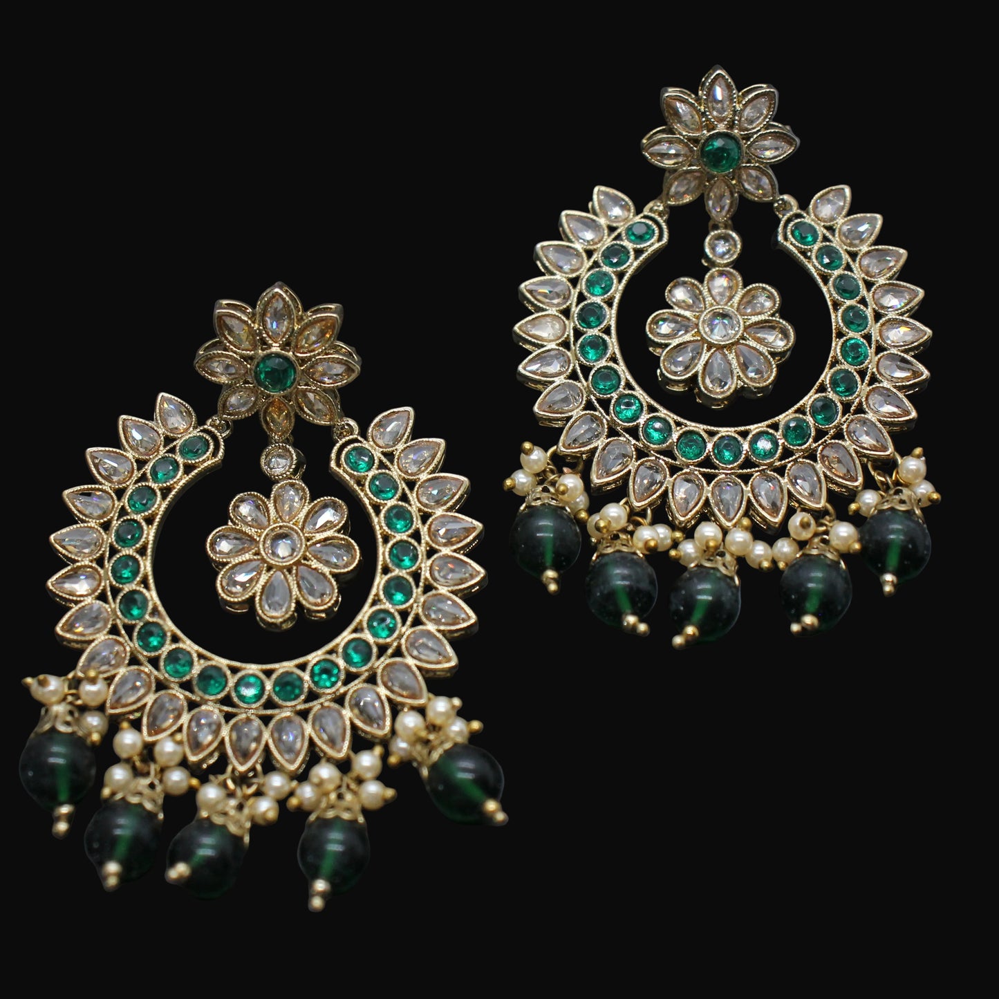 Ornate gold and green earrings on a dark background