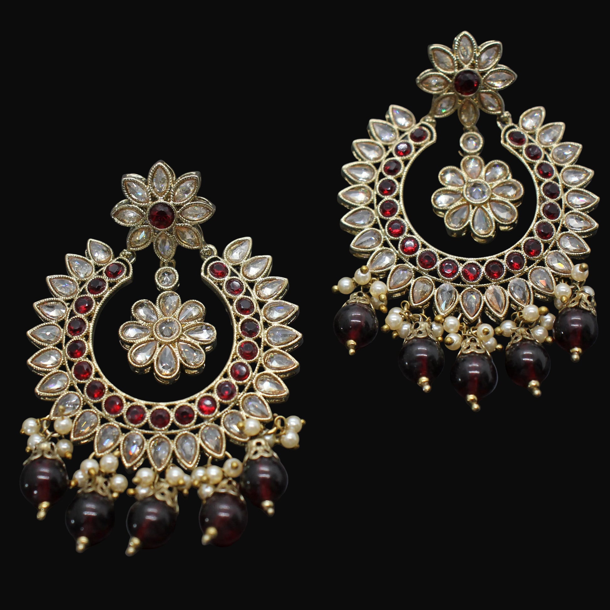 Ornate gold earrings with red and clear gemstones on a dark background
