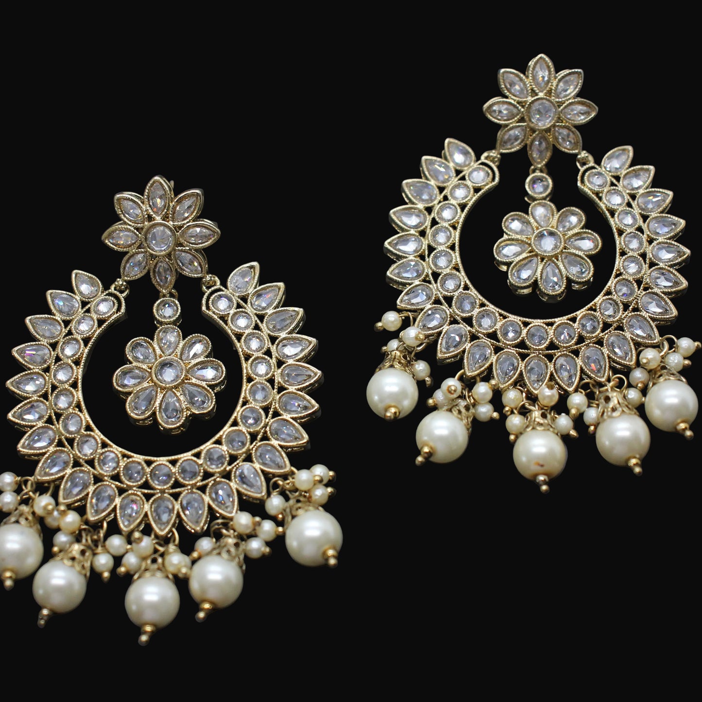 Pair of ornate gold and pearl earrings on a dark background