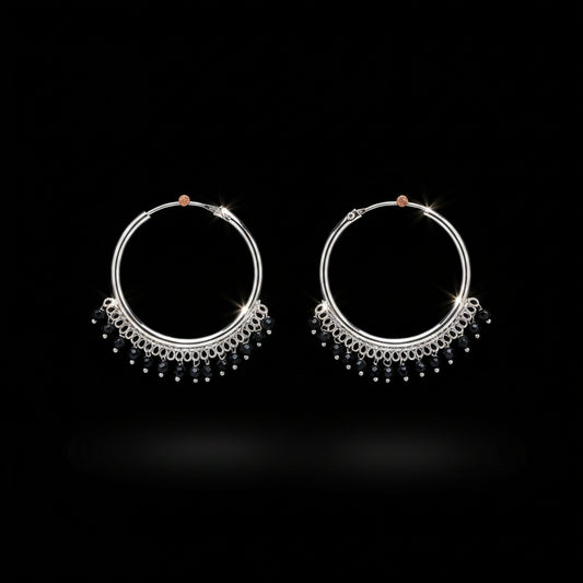 A pair of silver hoop earrings with dangling beaded fringe, displayed on a textured orange-brown background.