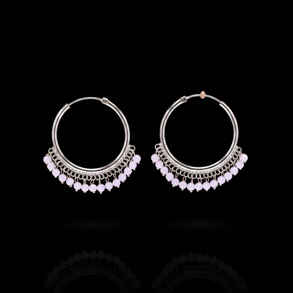 A pair of silver-tone hoop earrings with dangling beaded fringe in light pink, displayed on a textured brown background.