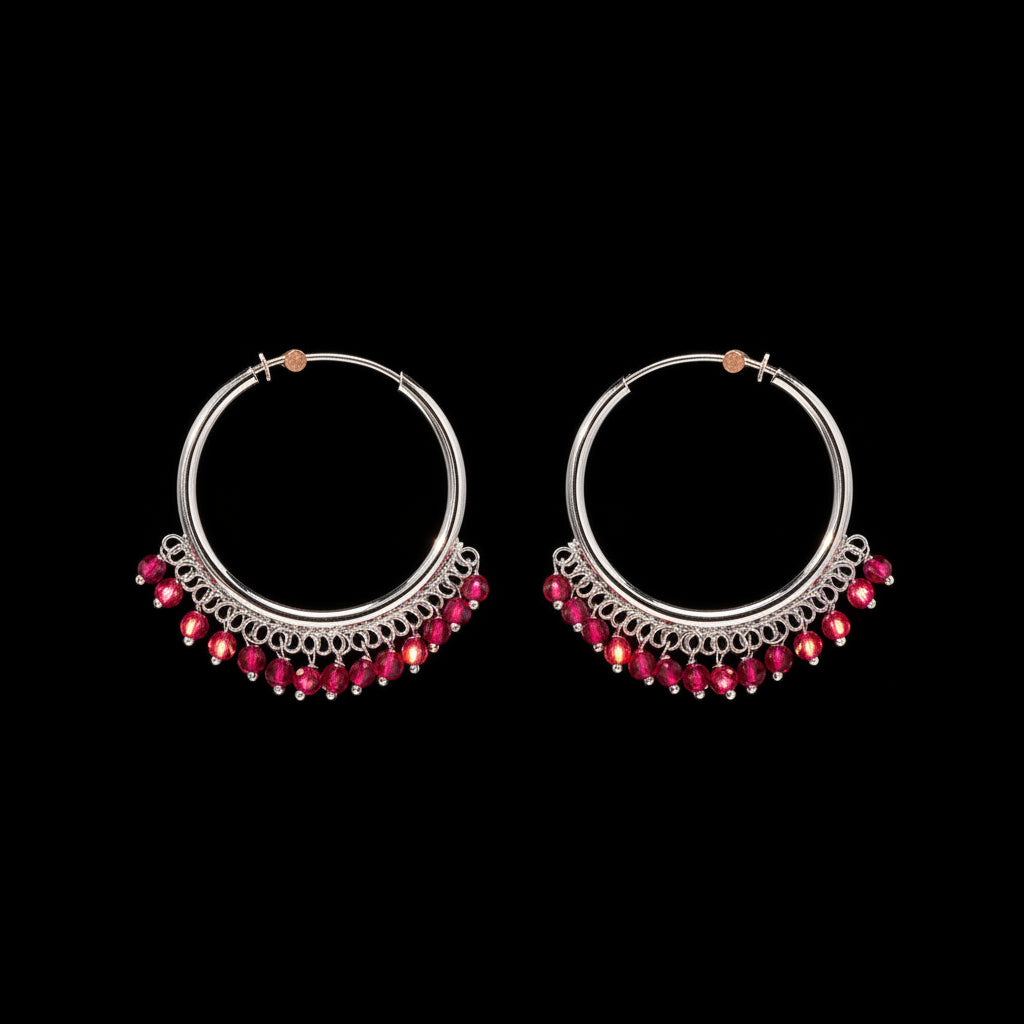 A pair of silver-toned hoop earrings with dangling rows of bright pink gemstones, displayed on a textured brown background.