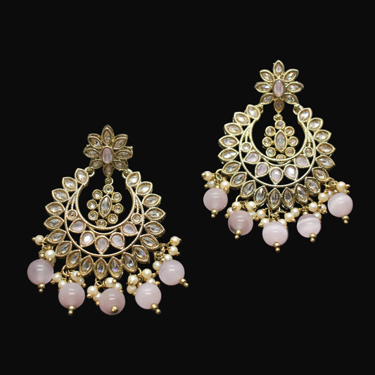 Ornate gold earrings with pink stones on a dark gray background