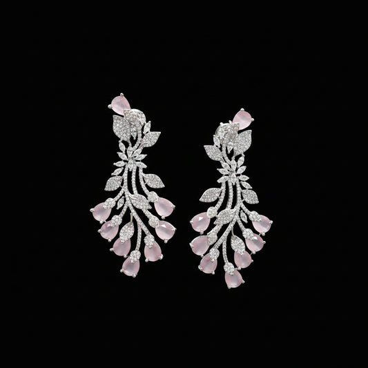 A pair of silver-toned dangle earrings decorated with pavé-set clear stones and pink teardrop gemstones, displayed on a dark gray background.