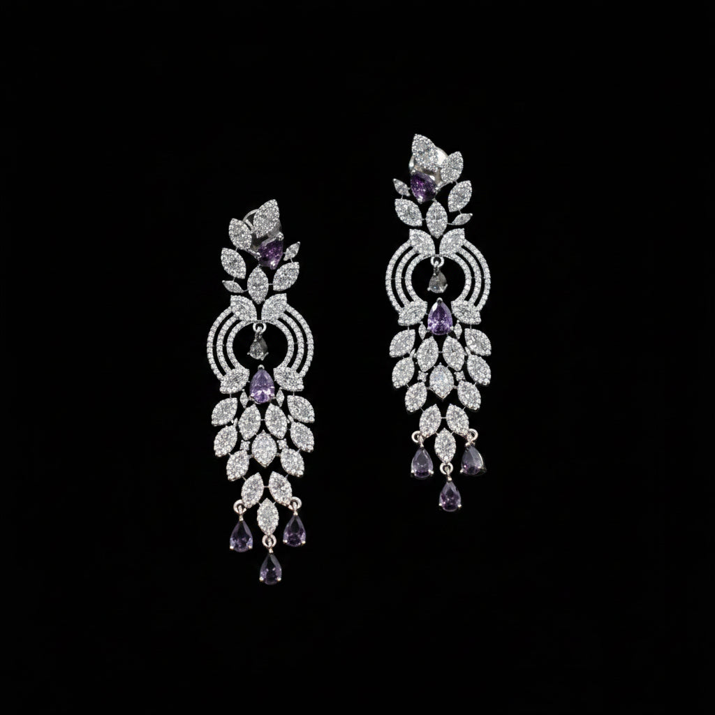 A pair of ornate silver-toned dangle earrings embellished with clear pavé stones and accented with purple amethyst teardrop and round stones, displayed on a dark gray background.