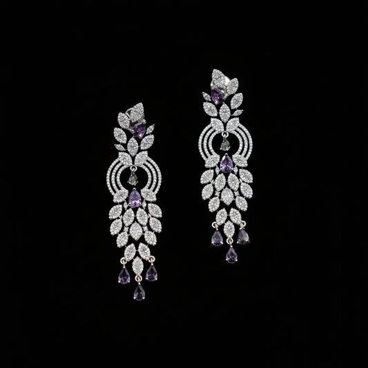 A pair of ornate silver-toned dangle earrings embellished with clear pavé stones and accented with purple amethyst teardrop and round stones, displayed on a dark gray background.