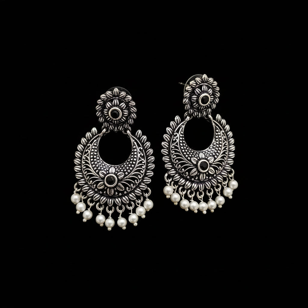 Ornate silver earrings with pearl drops on a gray background, featuring the brand 'Saheli'.