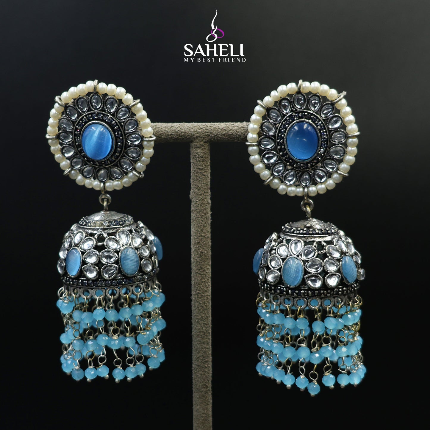 Pair of earrings with blue stones on a black background, featuring the brand 'Saheli'.