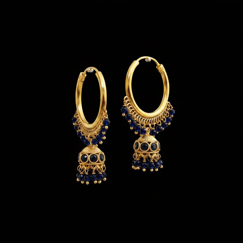A pair of gold-toned Jhumka earrings with dark blue stone accents, displayed on a gray stand. The brand logo 'SAHELI MY BEST FRIEND' is visible at the top center.