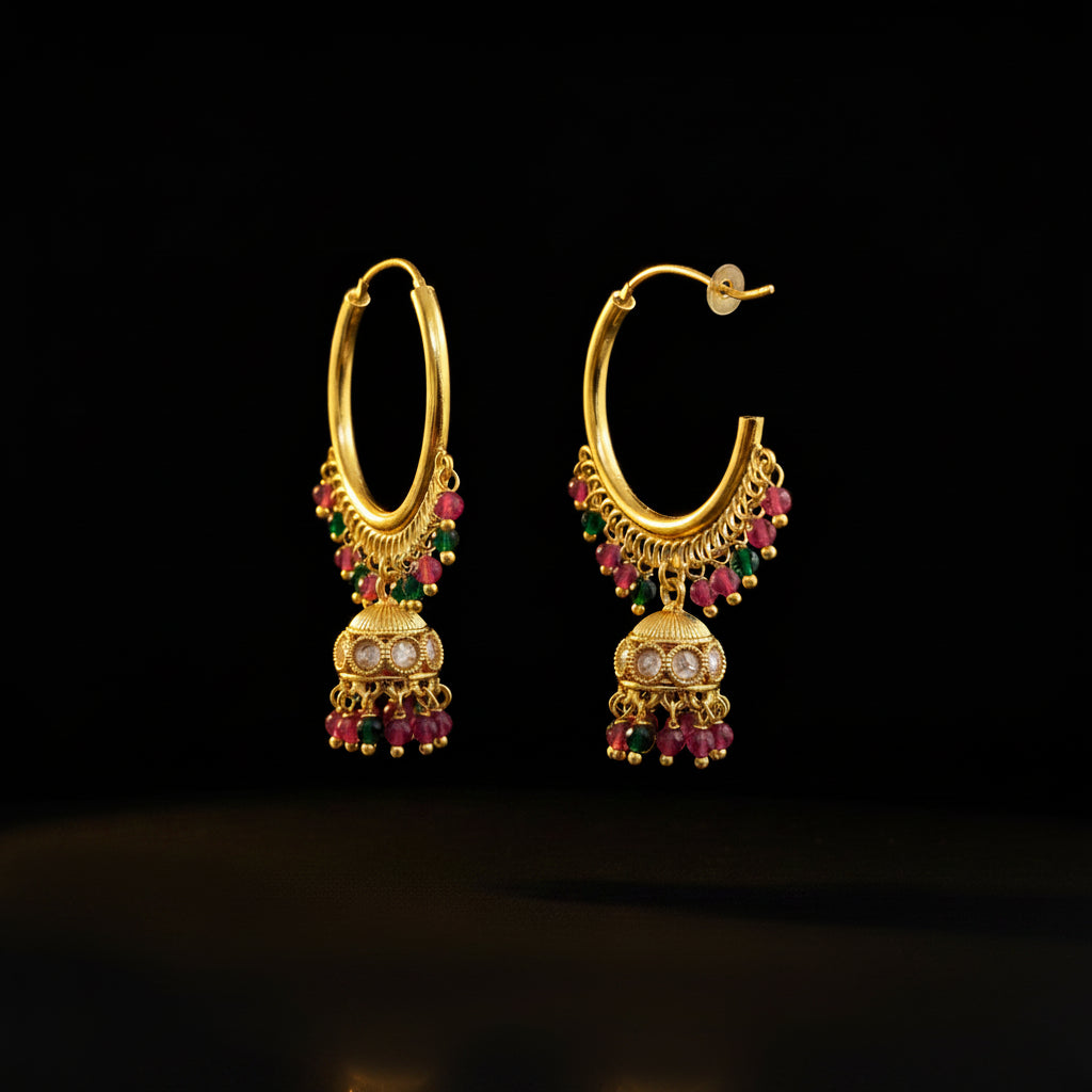 A pair of gold-toned traditional hoop earrings with dangling jhumka-style charms, decorated with pink and green beads and small clear stones, displayed on a gray jewelry stand against a gray background. The brand name 'SAHELI MY BEST FRIEND' is printed at the top.