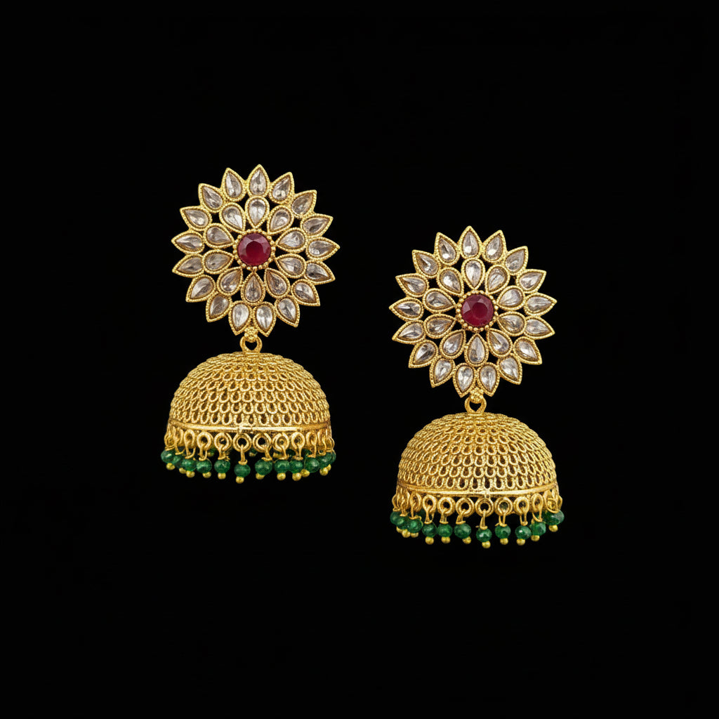 Gold jhumka earrings with red and green stones on a gray stand against a light blue background.