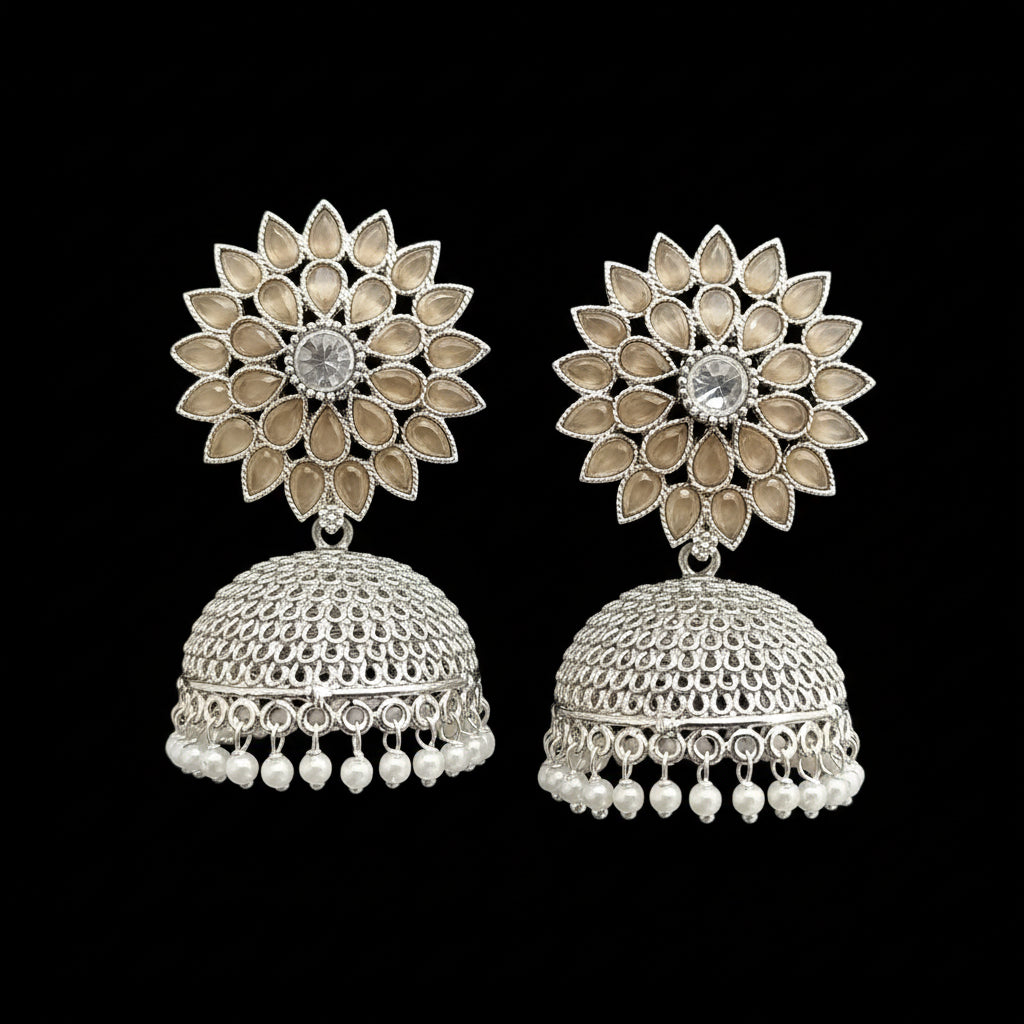 Silver floral jhumka earrings with pearl drops on a gray stand against a light blue background.