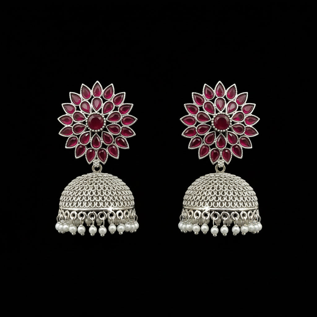 Pair of ornate earrings with floral design and pearl accents on a gray stand.