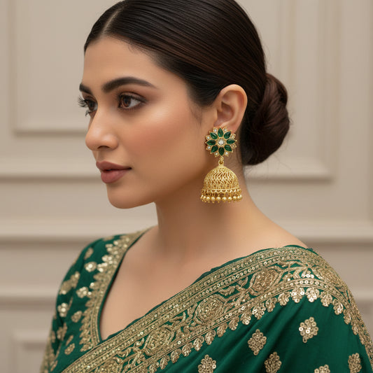 Gold and green jhumka earrings with 'Saheli' branding on a black background