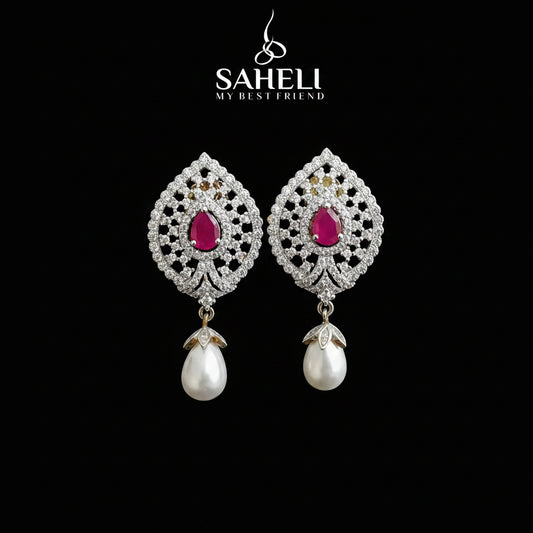 A pair of ornate silver-toned drop earrings with bright pink teardrop-shaped center stones and dangling white pearl drops, displayed on a black stand against a gray background. The brand name 'SAHELI MY BEST FRIEND' is visible at the top.