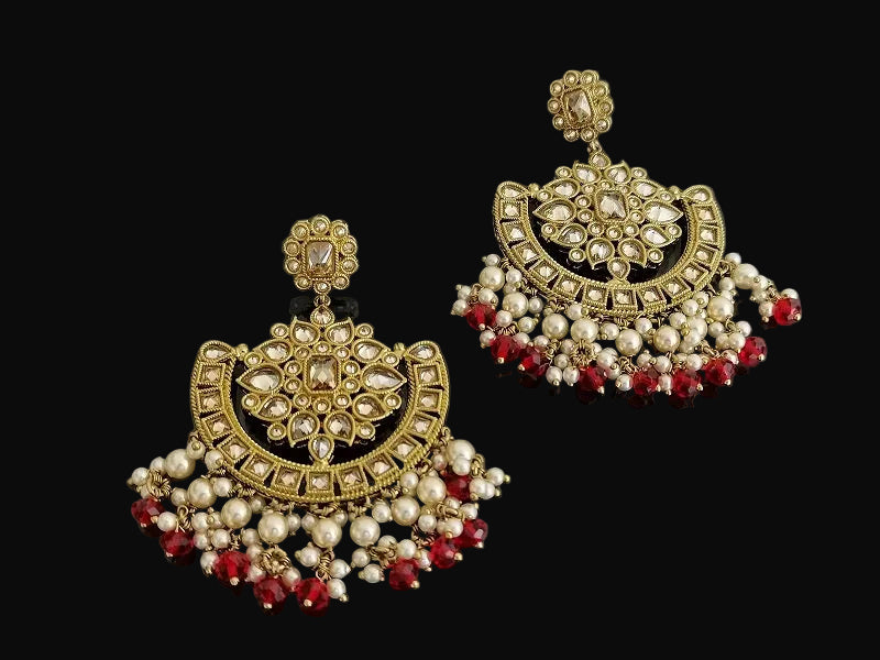 Pair of ornate earrings with gold, pearls, and red stones on a dark background