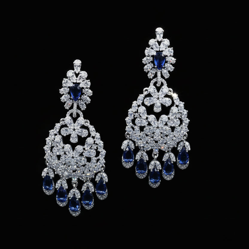 Pair of silver earrings with blue stones on a black stand, branded 'Sahelli'.