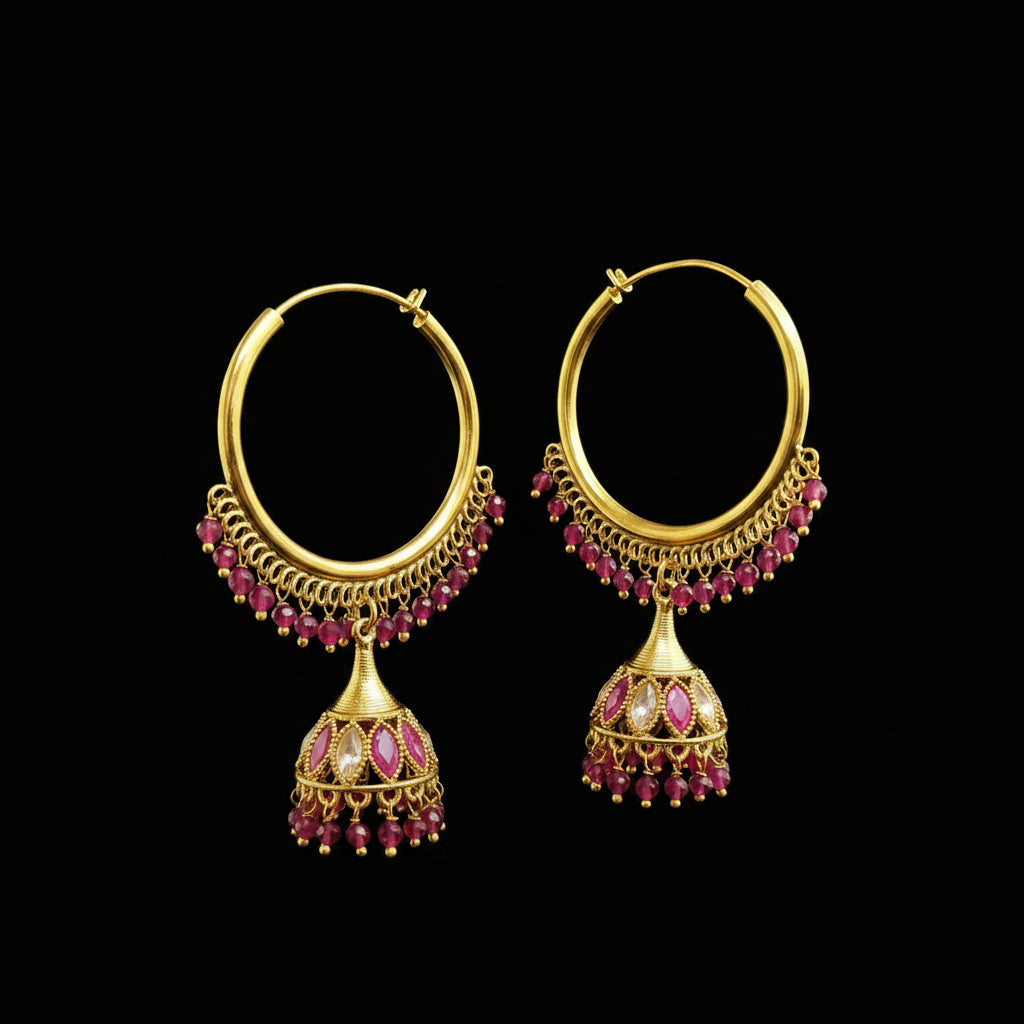A pair of gold-toned hoop earrings with dangling jhumka-style bells, decorated with small pink gemstones and clear stones, displayed on a gray jewelry stand against a light gray background.