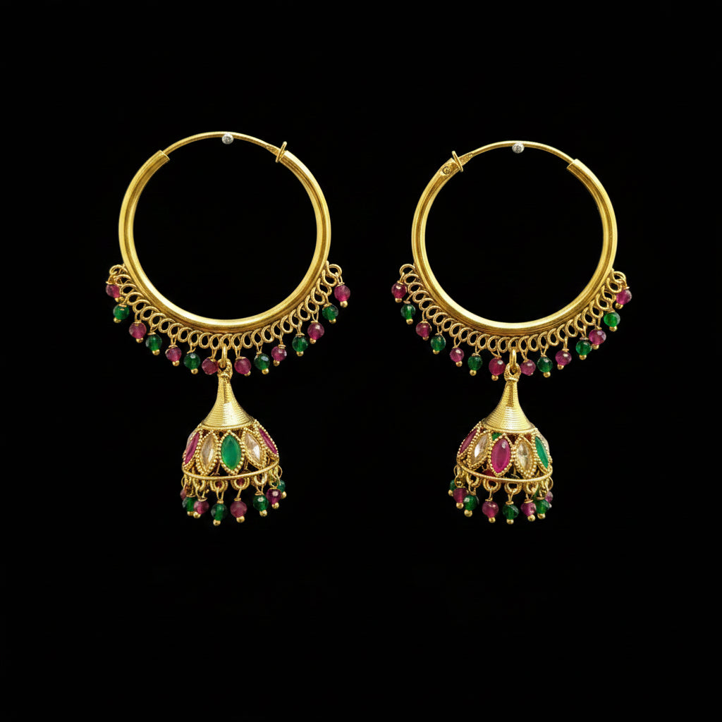 A pair of gold-toned traditional hoop earrings with dangling bell-shaped charms, decorated with small green and pink gemstones, displayed on a gray stand.