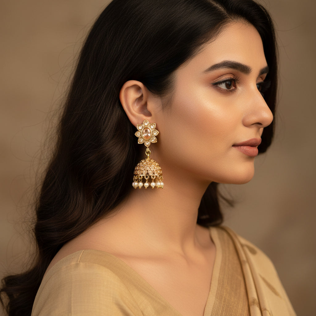 Gold and pearl earrings on a black stand with 'SAHELI' branding.