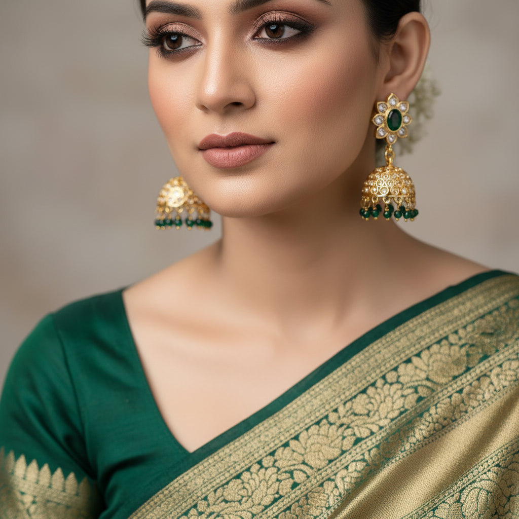 Gold and green gemstone earrings on a black stand with 'SAHELI' branding.