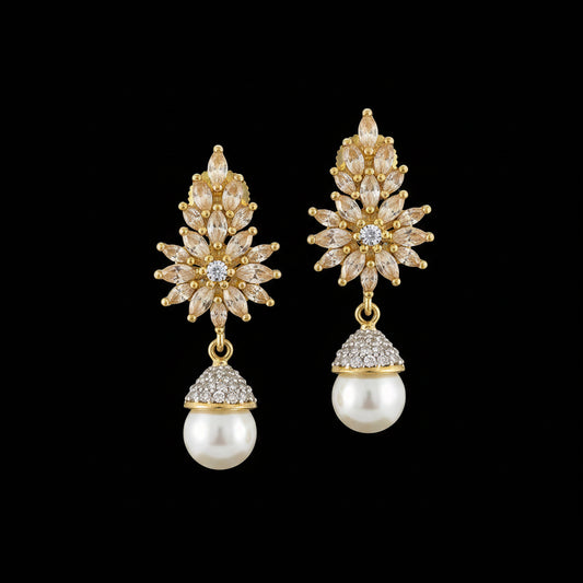 A pair of gold-plated dangle earrings with floral starburst designs, clear rhinestone accents, and white pearl drops, displayed on a dark reflective surface. The brand logo 'SAHELI MY BEST FRIEND' is visible in the top left corner.