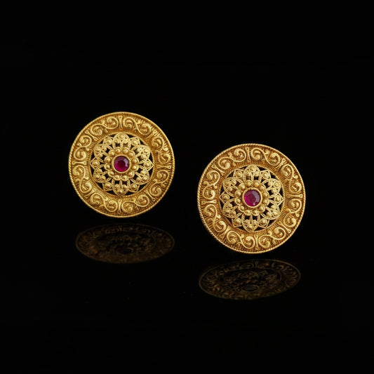 Pair of gold earrings with red gemstones on a dark surface