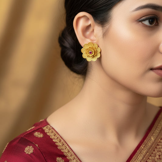 Pair of gold flower-shaped earrings with red gemstones on a dark background