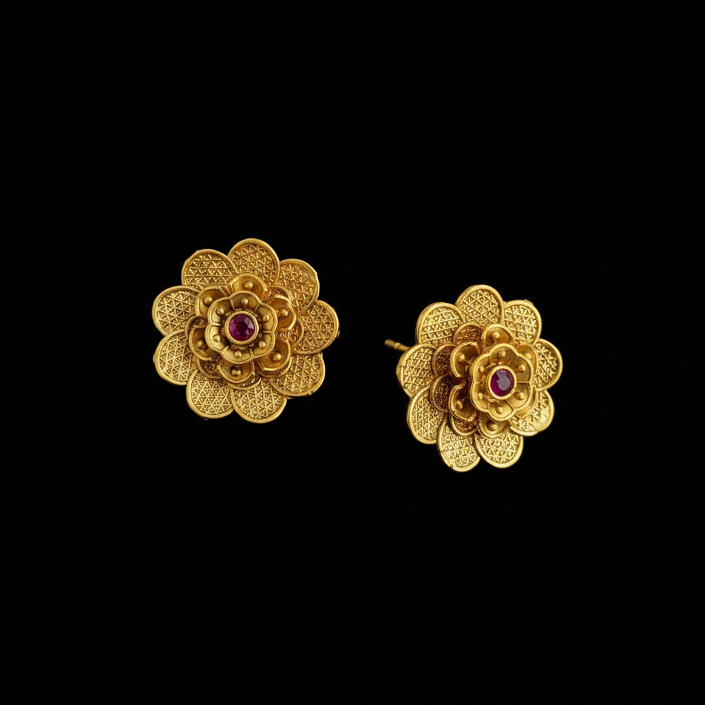 Pair of gold flower-shaped earrings with red gemstones on a dark background