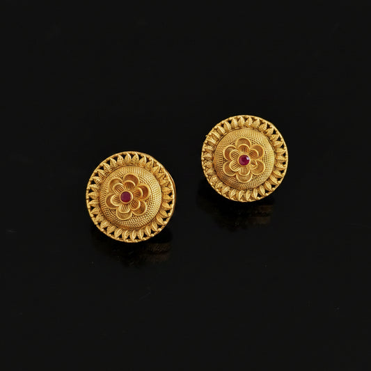 Pair of gold earrings with floral design and red gemstones on a black background