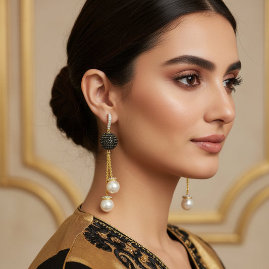 Pair of earrings with pearls and gemstones on a dark background, branded 'Saheli'.