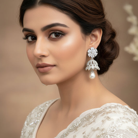 Pair of silver earrings with floral designs and pearl drops on a black stand.