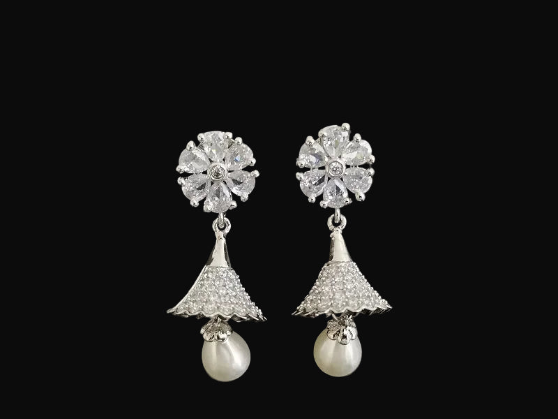 Pair of silver earrings with floral top and pearl drop on a black background