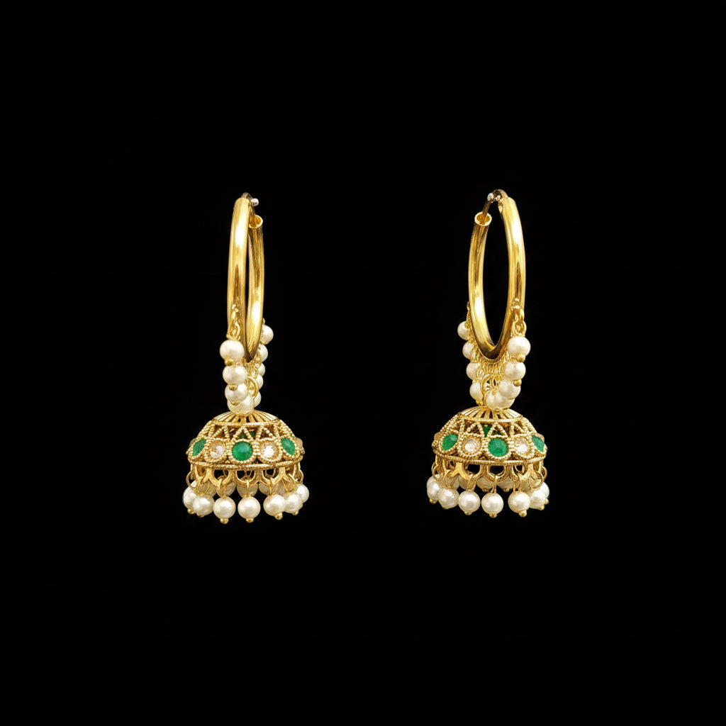 A pair of gold-toned Indian jhumka earrings with white pearl bead drops and green stone accents, displayed on a black jewelry stand against a gray background.