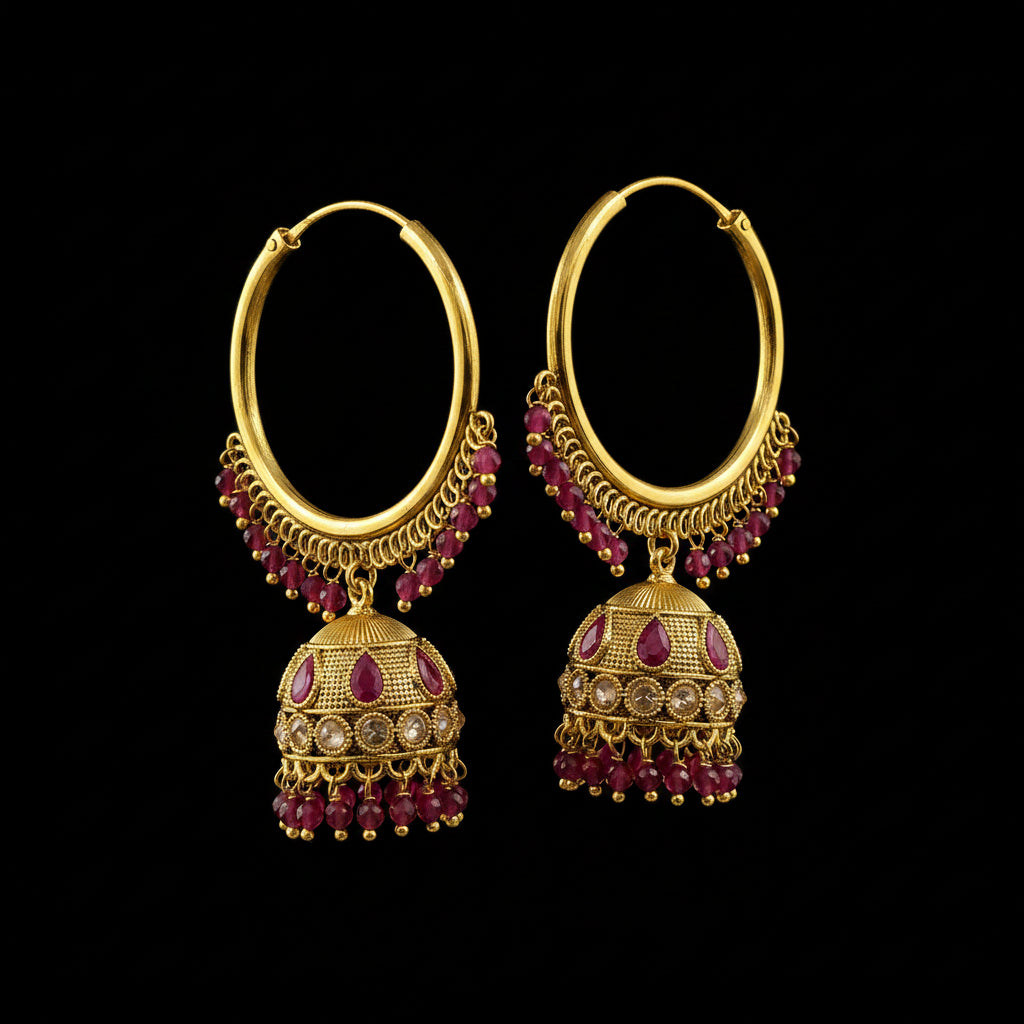 A pair of gold-toned traditional hoop earrings with dangling bell-shaped charms, decorated with pink gemstones and small clear stones, displayed on a gray jewelry stand.
