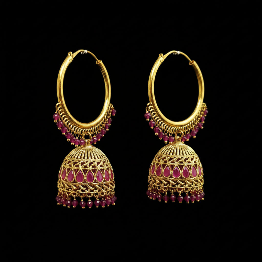 A pair of gold-toned traditional hoop earrings with dangling bell-shaped jhumka elements, decorated with pink gemstone inlays and small pink bead chains, displayed on a gray stand.
