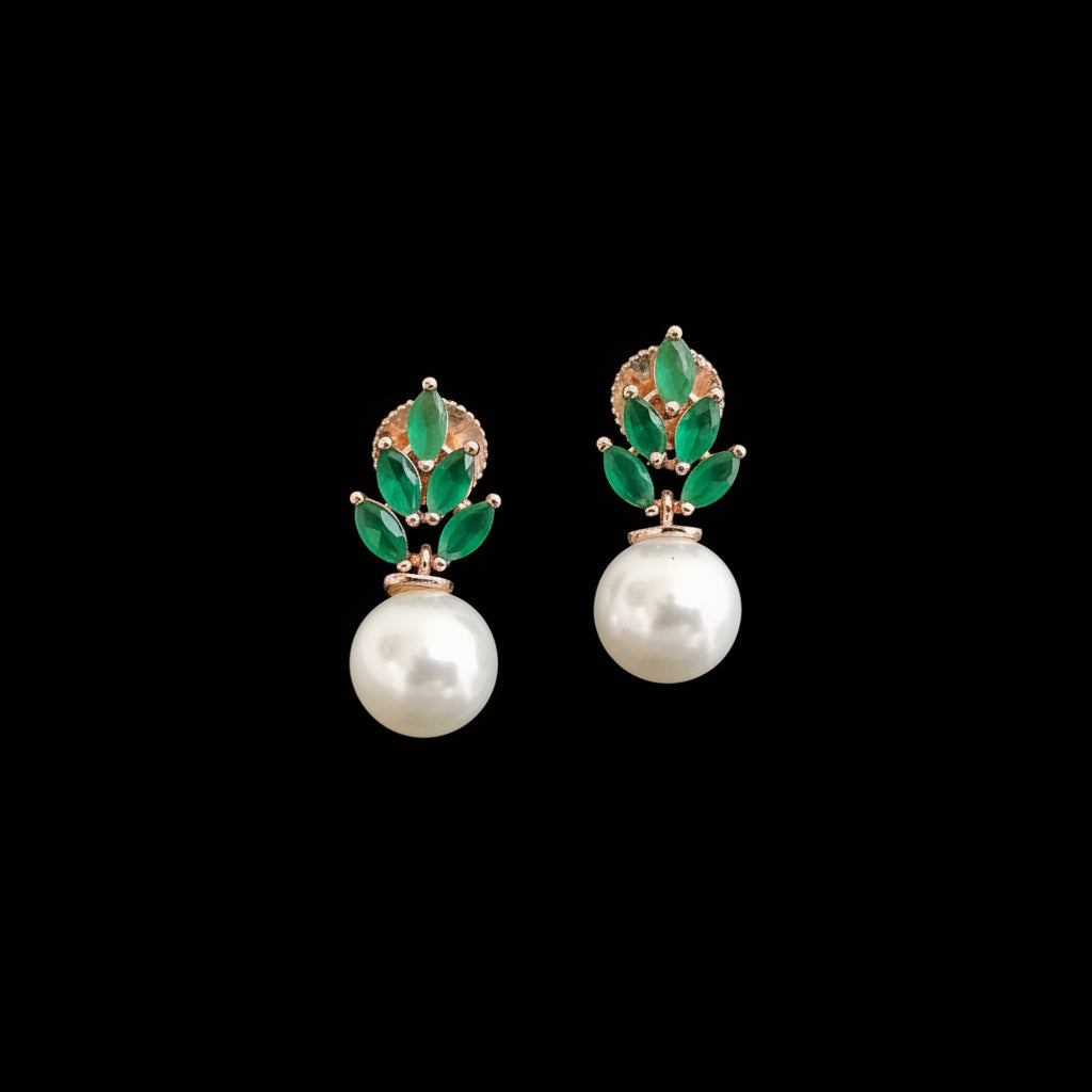 A pair of gold and green gemstone drop earrings with white pearl drops, displayed on a black textured stand against a neutral gray background.