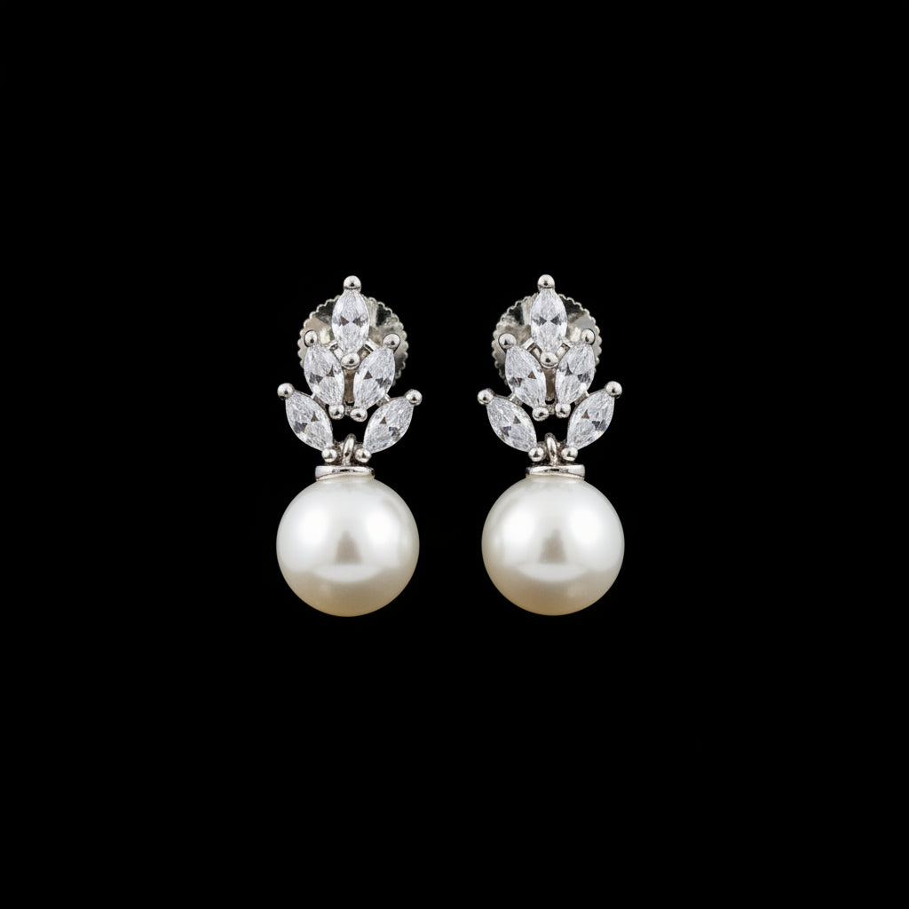 A pair of silver-tone drop earrings with clear marquise and round crystals above large white pearl drops, displayed on a black jewelry stand against a dark gray background.