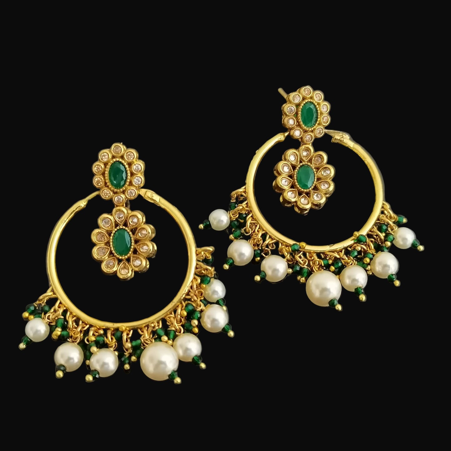 Gold earrings with green and pearl accents on a dark background