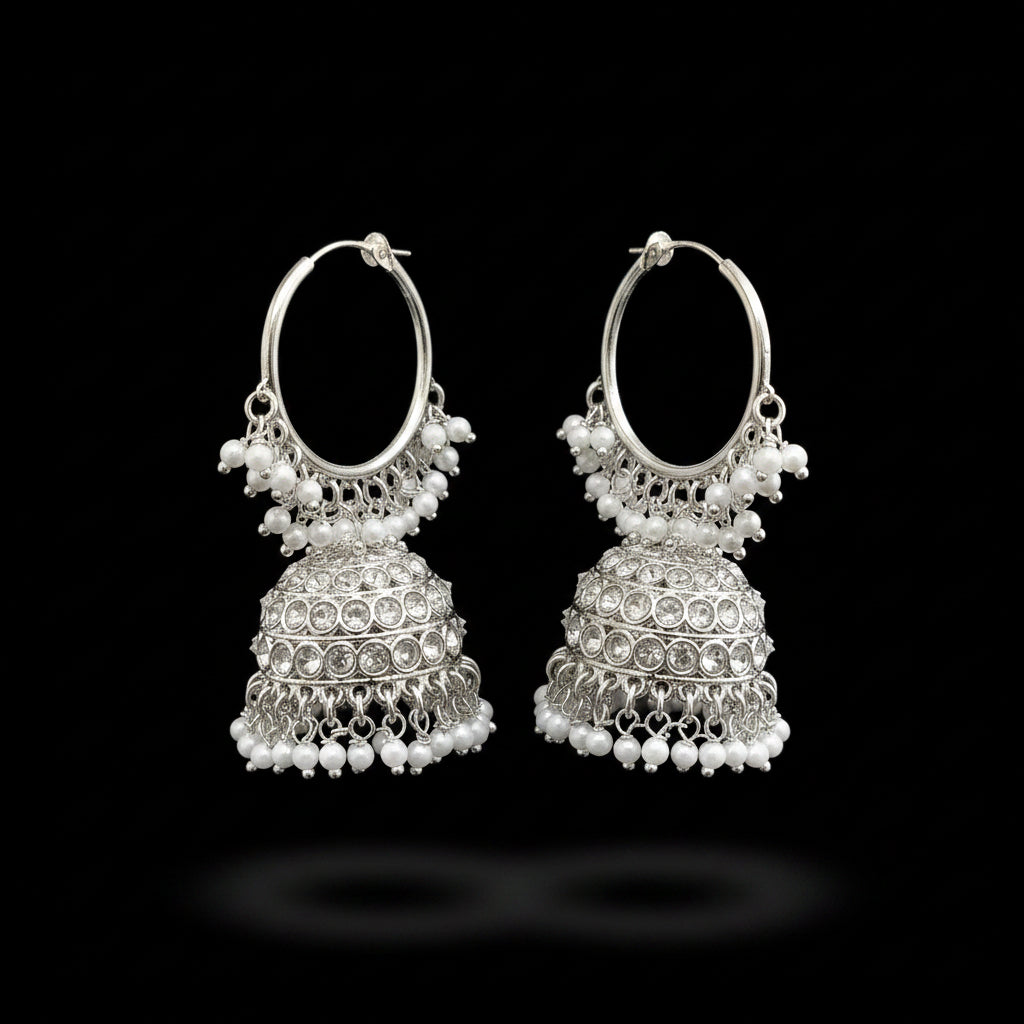 A pair of silver-toned jhumka earrings with dangling pearl bead chains, displayed on a dark gray stand against a dark gray background.