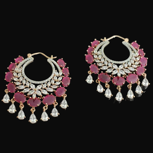 Pair of ornate earrings with red gemstones and gold accents on a dark background, branded 'Saheli'.