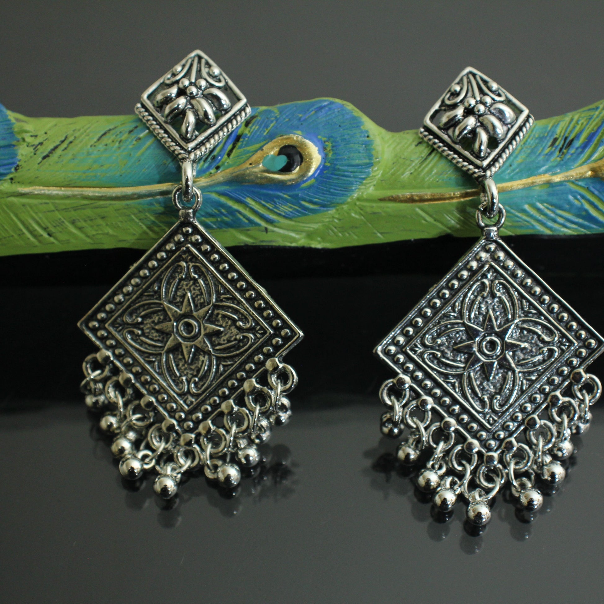 Pair of silver earrings on a green ribbon with peacock feathers