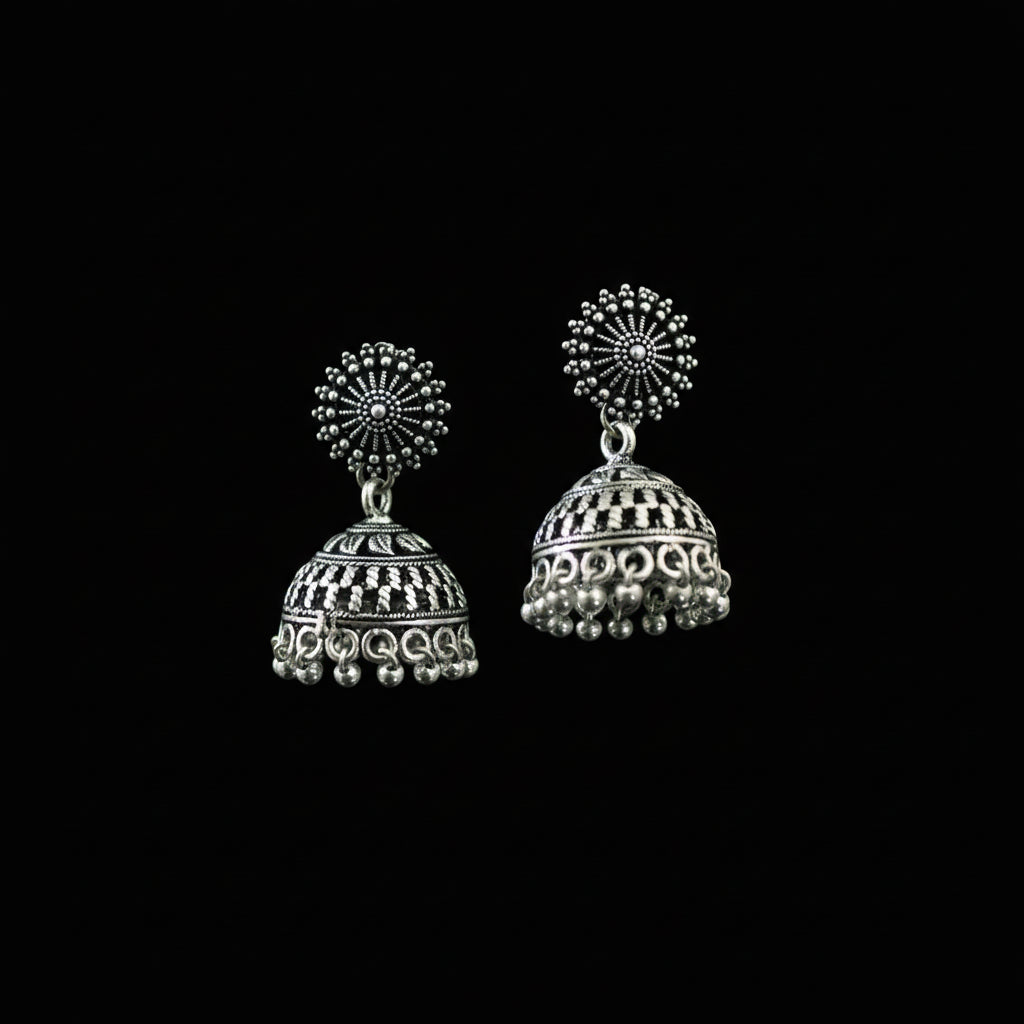 Silver jhumka earrings on a decorative green and blue feather against a dark background