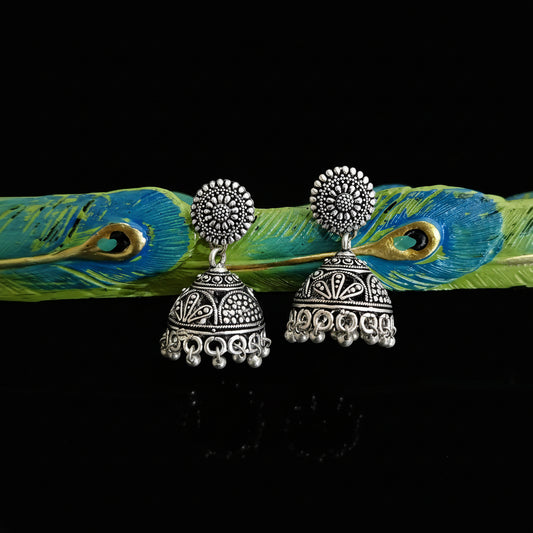 Silver earrings on a peacock feather with a gray background