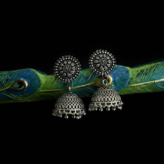 Pair of silver earrings on a decorative branch with peacock feathers