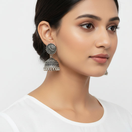 Pair of silver bell-shaped earrings on a decorative branch with a gray background