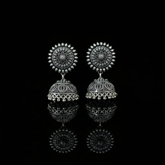 Silver earrings on a peacock feather with a dark background