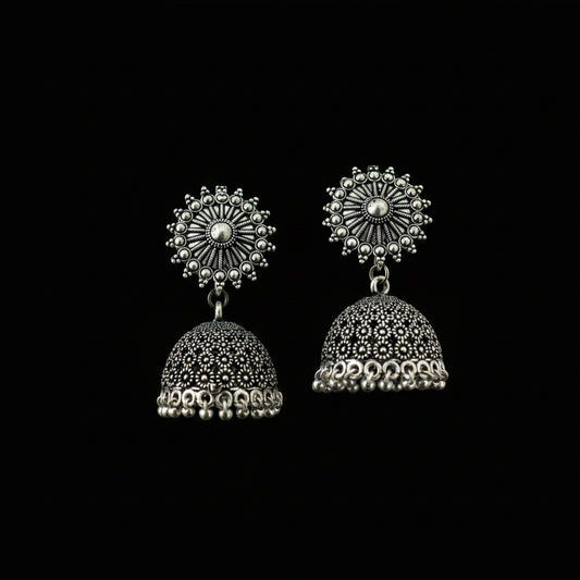 Pair of silver jhumka earrings on a decorative leaf