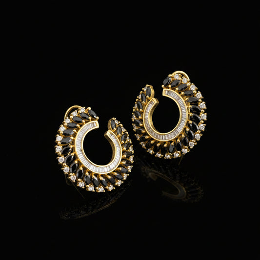 A pair of gold crescent-shaped hoop earrings adorned with clear crystals and dark marquise-cut stones, displayed on a dark reflective surface with the brand logo 'SAHELL MYBESTFRIEND' visible above.