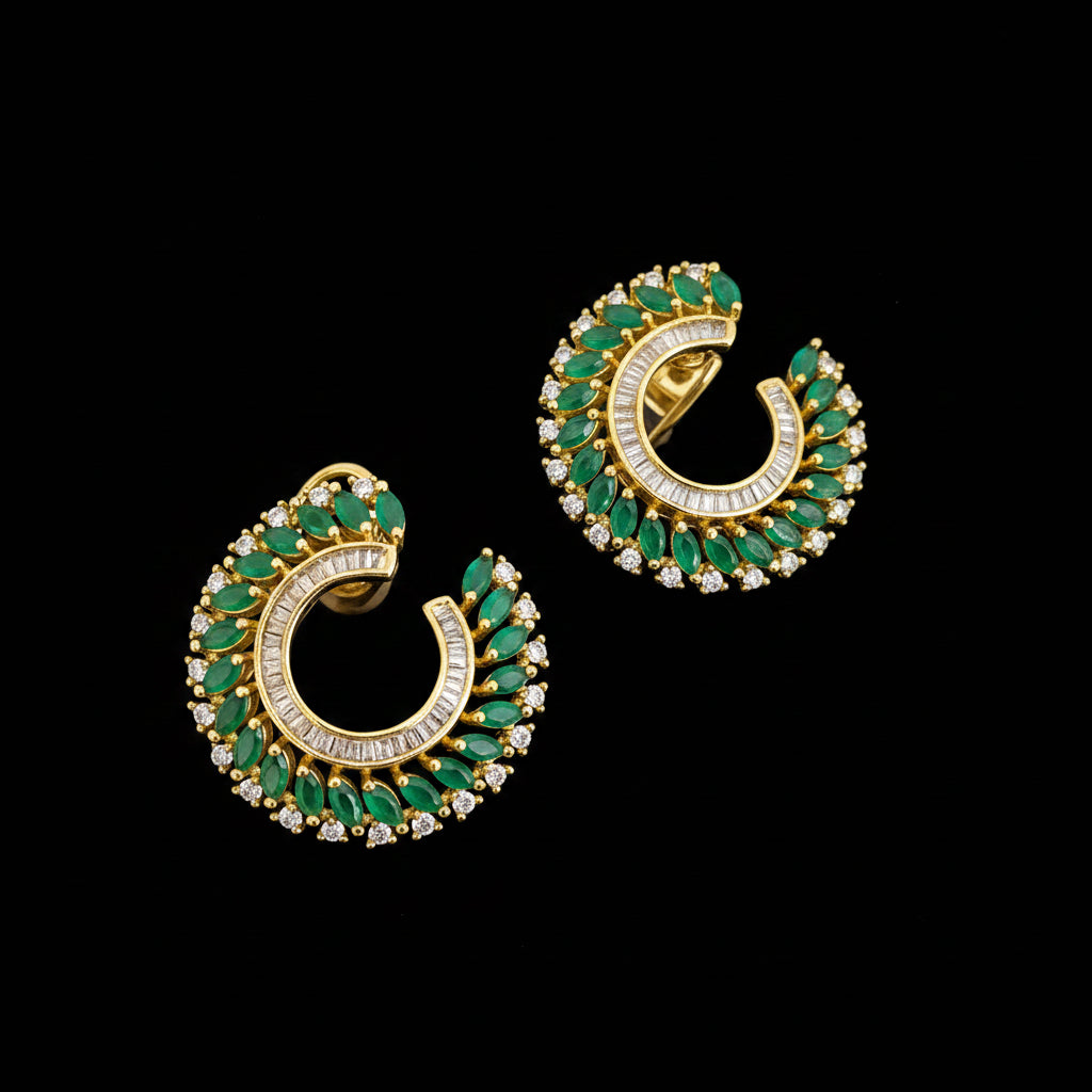 A pair of gold crescent-shaped hoop earrings decorated with green rectangular stones and small clear stones, displayed on a dark reflective surface with the brand name SAHELI MY BEST FRIEND visible in the upper left.